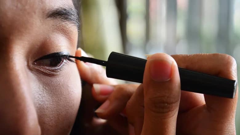 A woman applying eyeliner to her hooded eyes