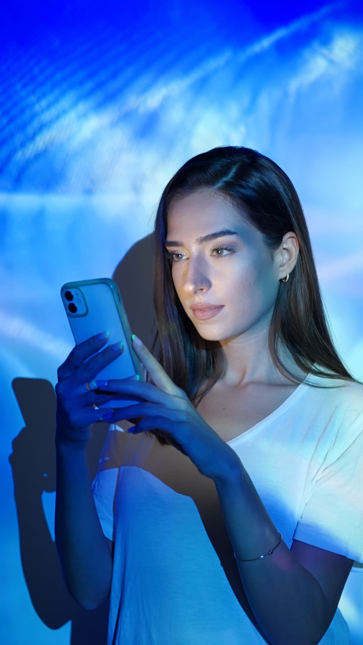 A woman looks at her phone screen with blue light background
