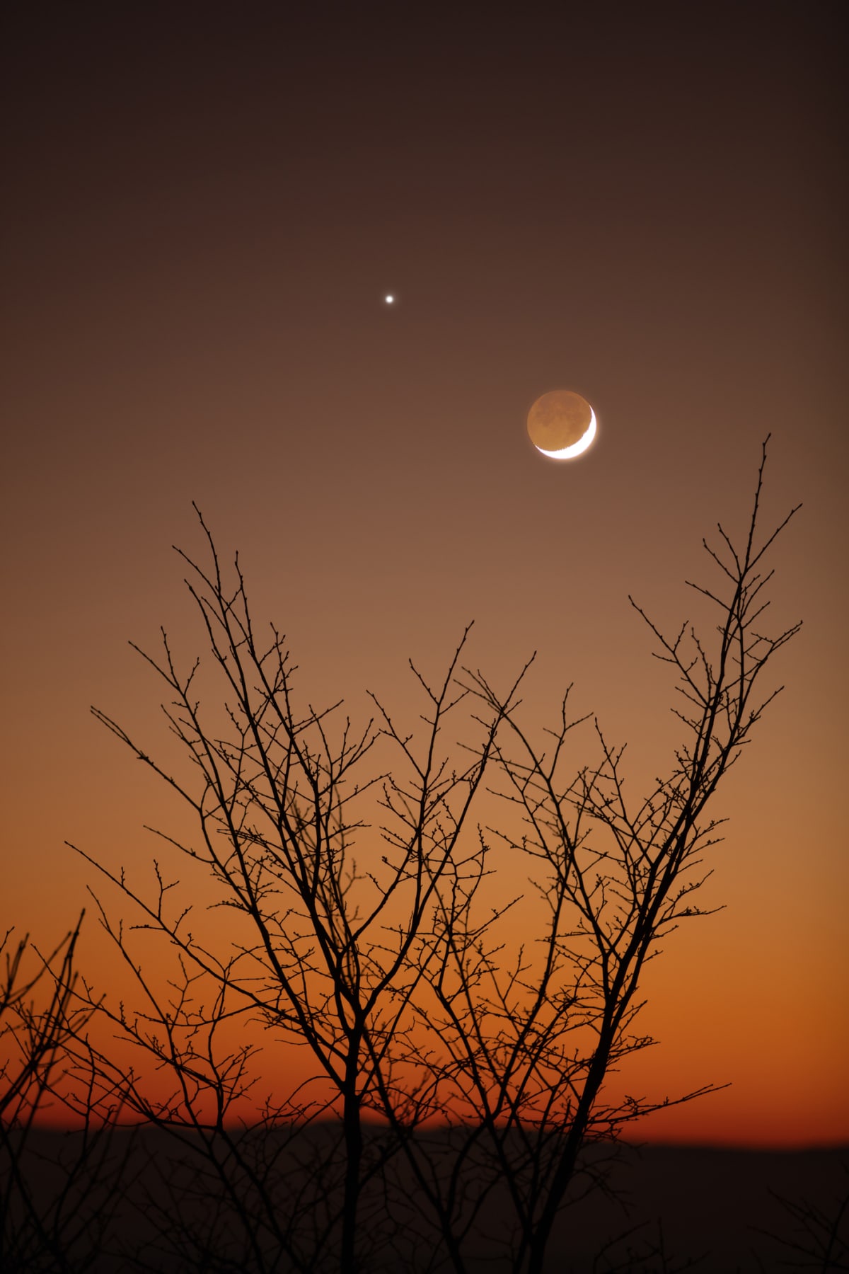 The moon and Saturn visible in a night sky with an orange hue
