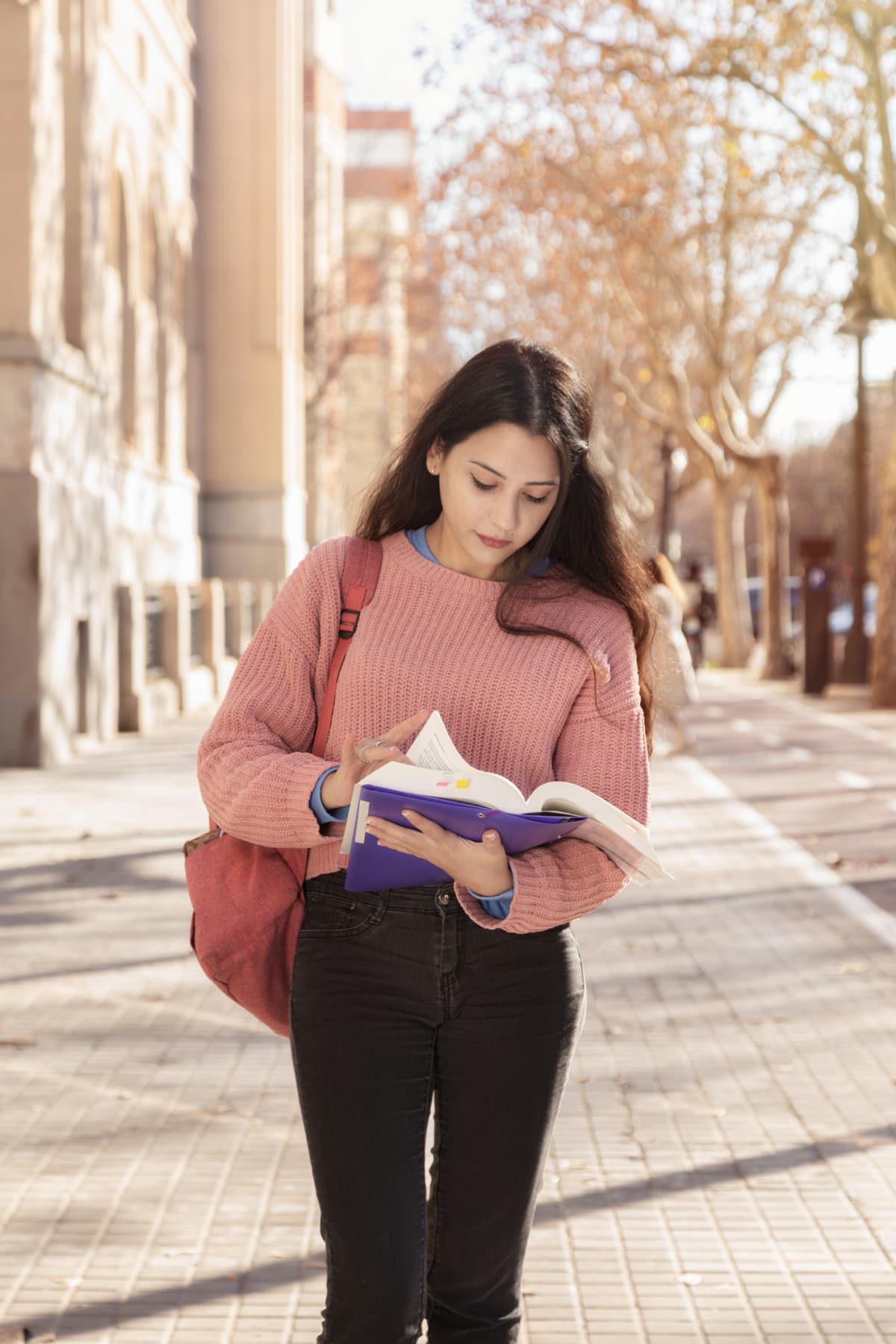Concentrated woman studying for college. Student girl reading a book on the street. Back to class. Pink color
