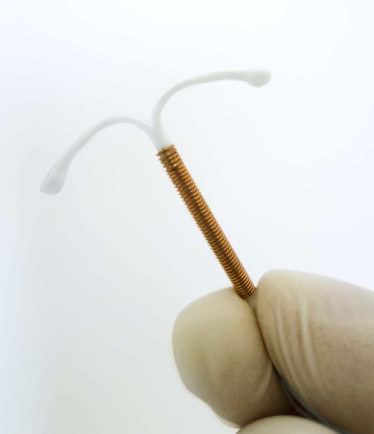 An IUD is held up by gloved fingers