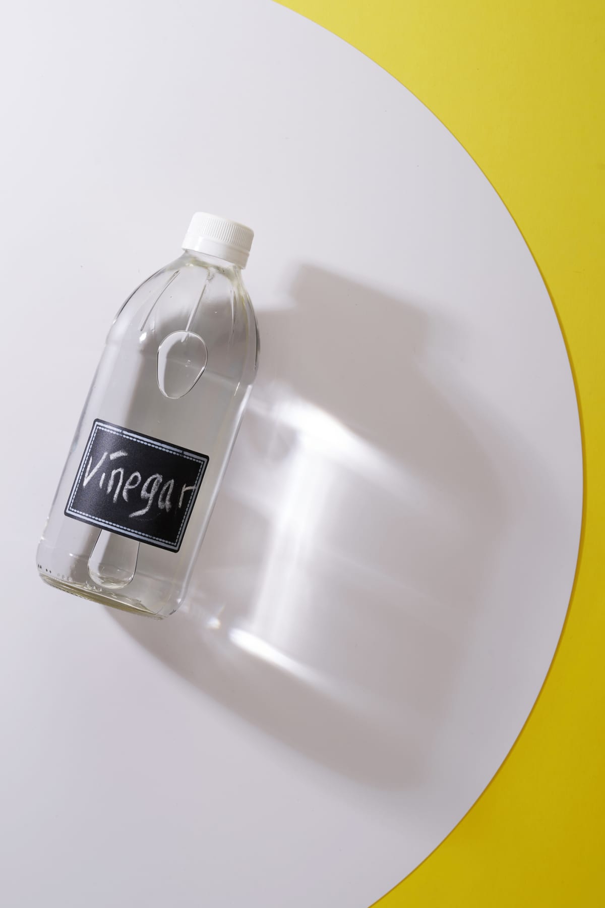 A clear bottle of white vinegar in front of a white and yellow background