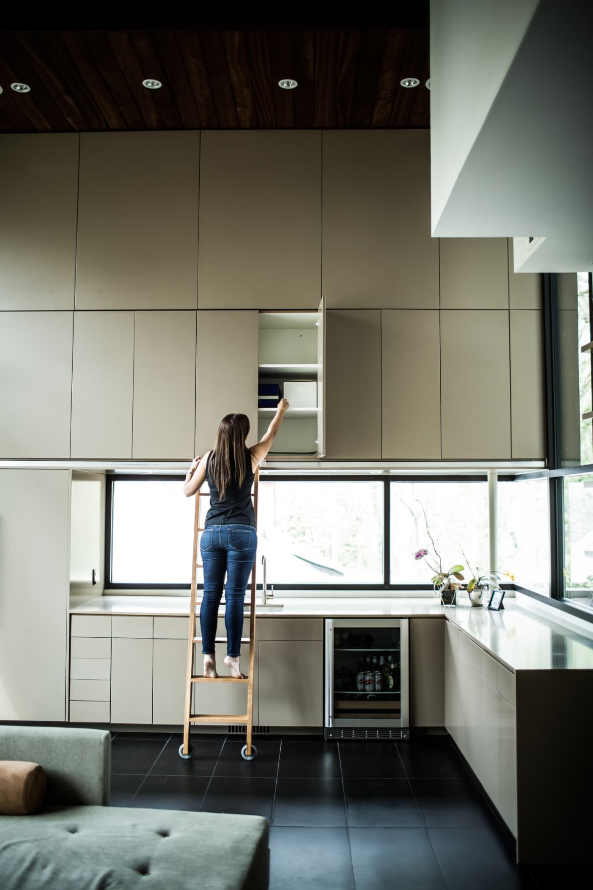 Woman on ladder reaching high cabinet