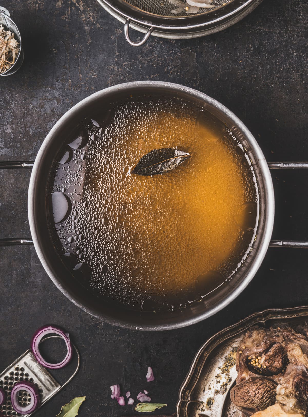 Clear beef bone broth or stock without meat in a pot on a dark rustic background