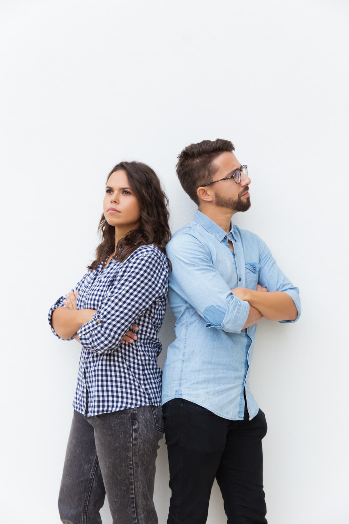 Sad unhappy couple standing back-to-back with arms crossed. Young woman in casual and man in glasses in glasses posing isolated over white background. Breakup concept