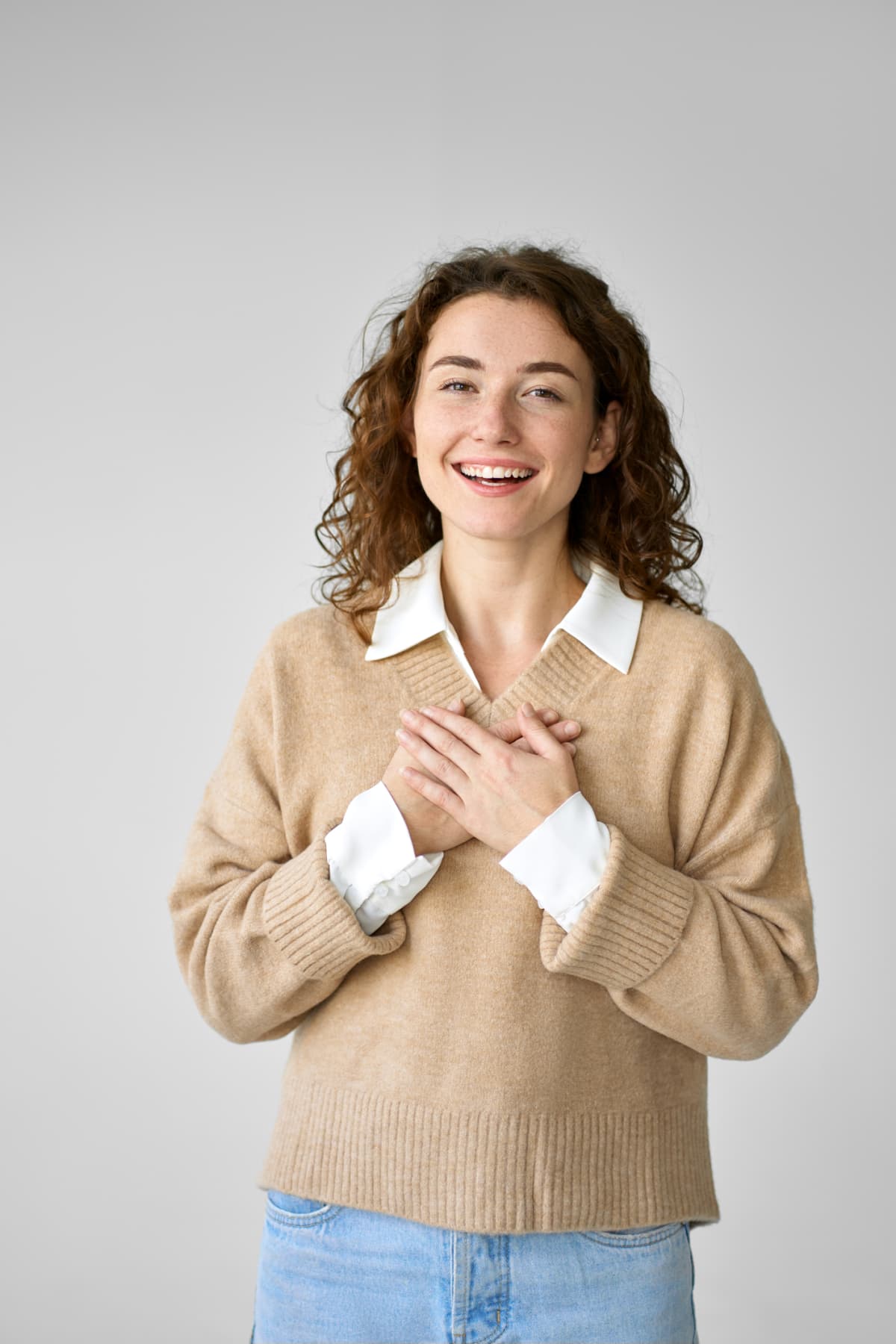 Happy pleased pretty young woman holding hands on chest feeling gratitude, mental balance, expressing thanking, kindness and love in heart standing isolated at white background.