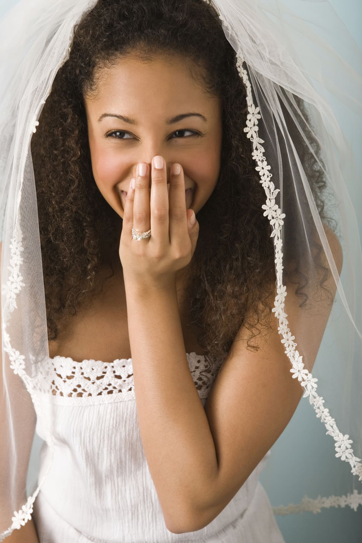 Teenage girl (16-17) wearing veil and wedding dress, laughing.
