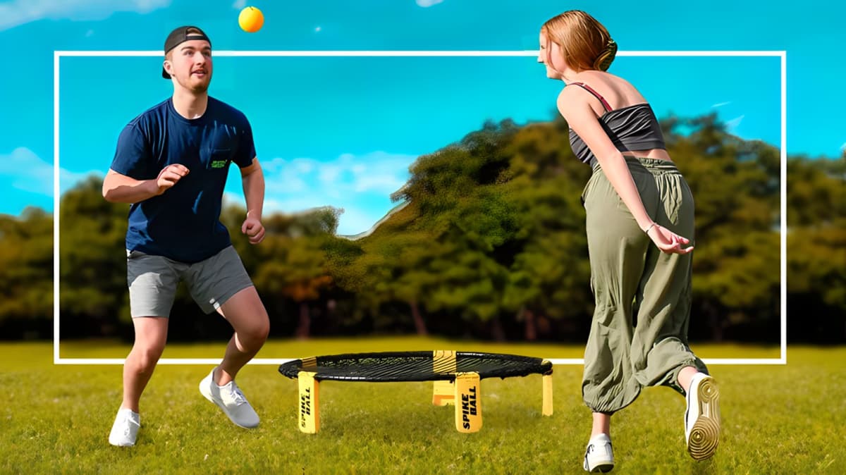 A young man looking at a yellow ball bouncing in the air while playing Spikeball