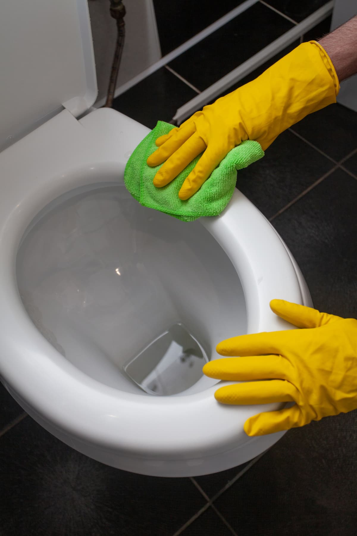 Hands of man in yellow gloves cleaning toilet bowl using cloth and detergent, concept for house cleaning and household duties