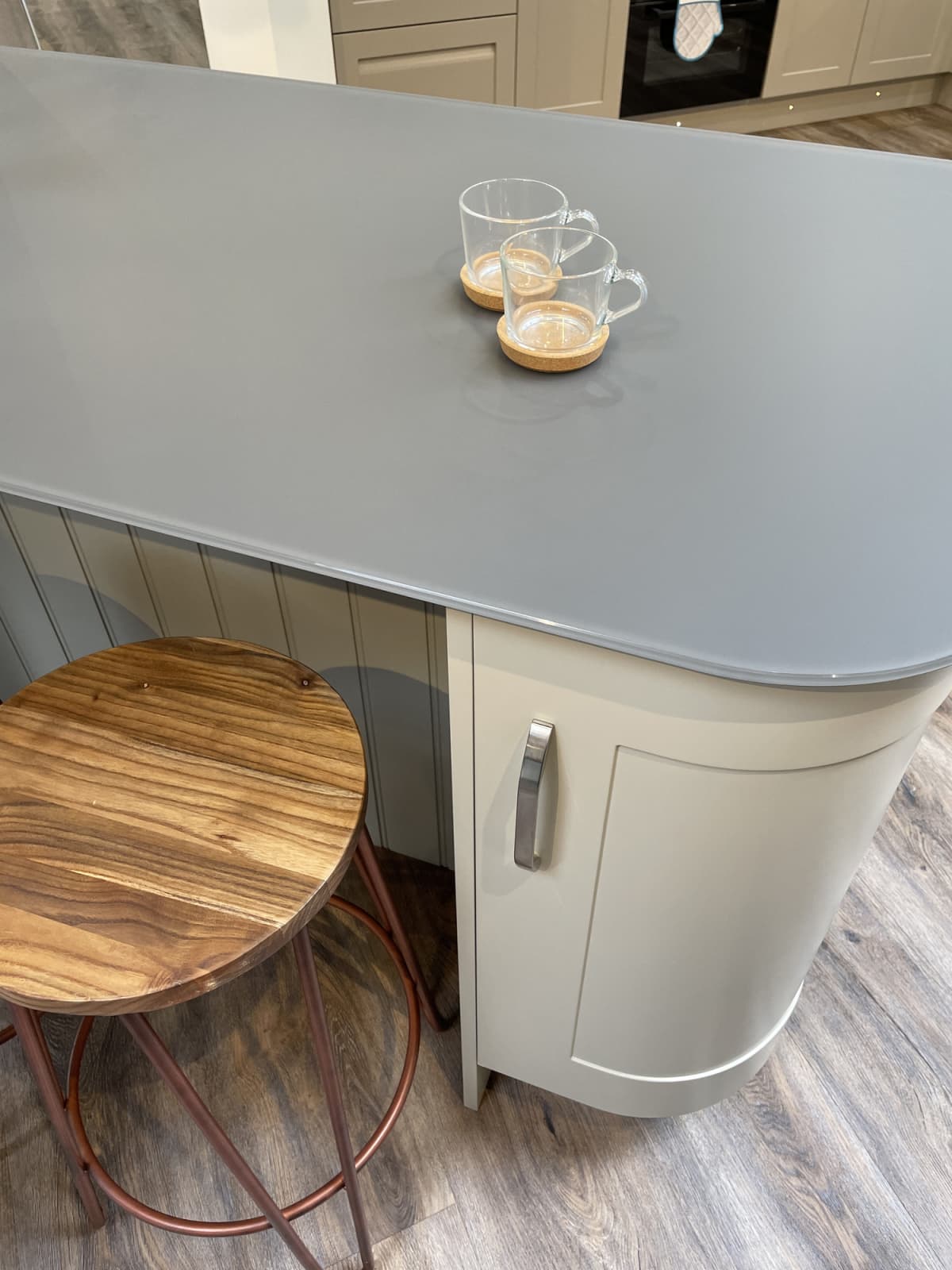 Stock photo showing curved breakfast bar cabinets painted duck egg blue with tongue and groove cladding timber and grey composite corian countertop, An oak wood stool with copper coloured metal legs can be seen on the dark oak effect laminate flooring.