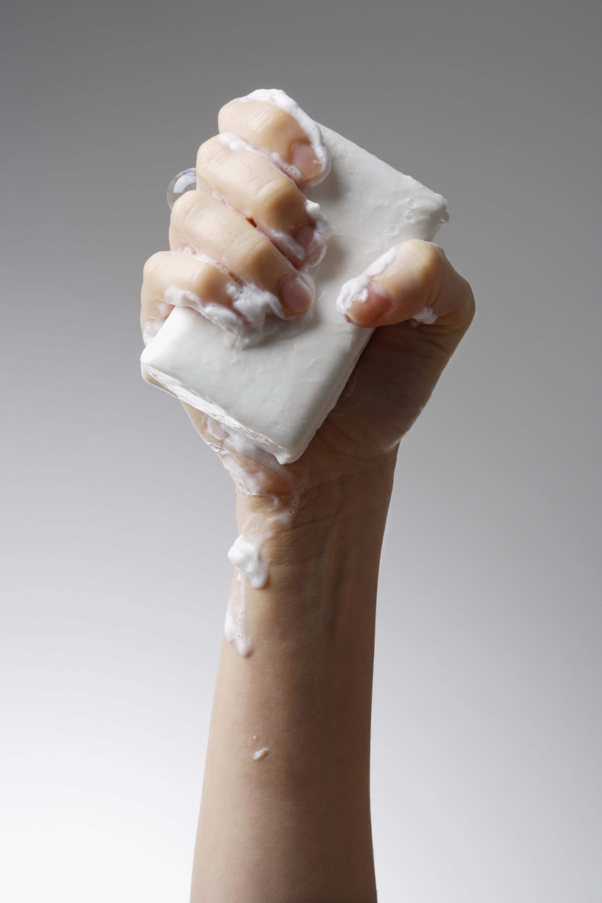 A hand holding up a foaming white soap bar.