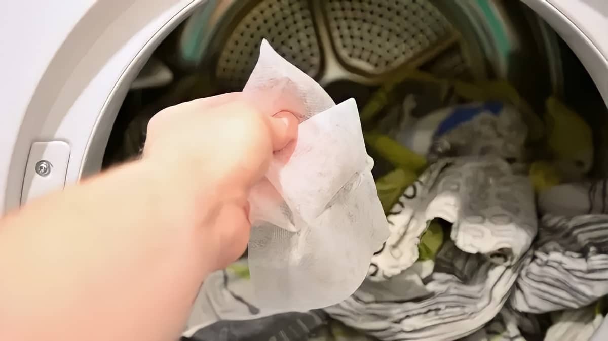 A person putting a dryer sheet into a dryer with clothes in the dryer