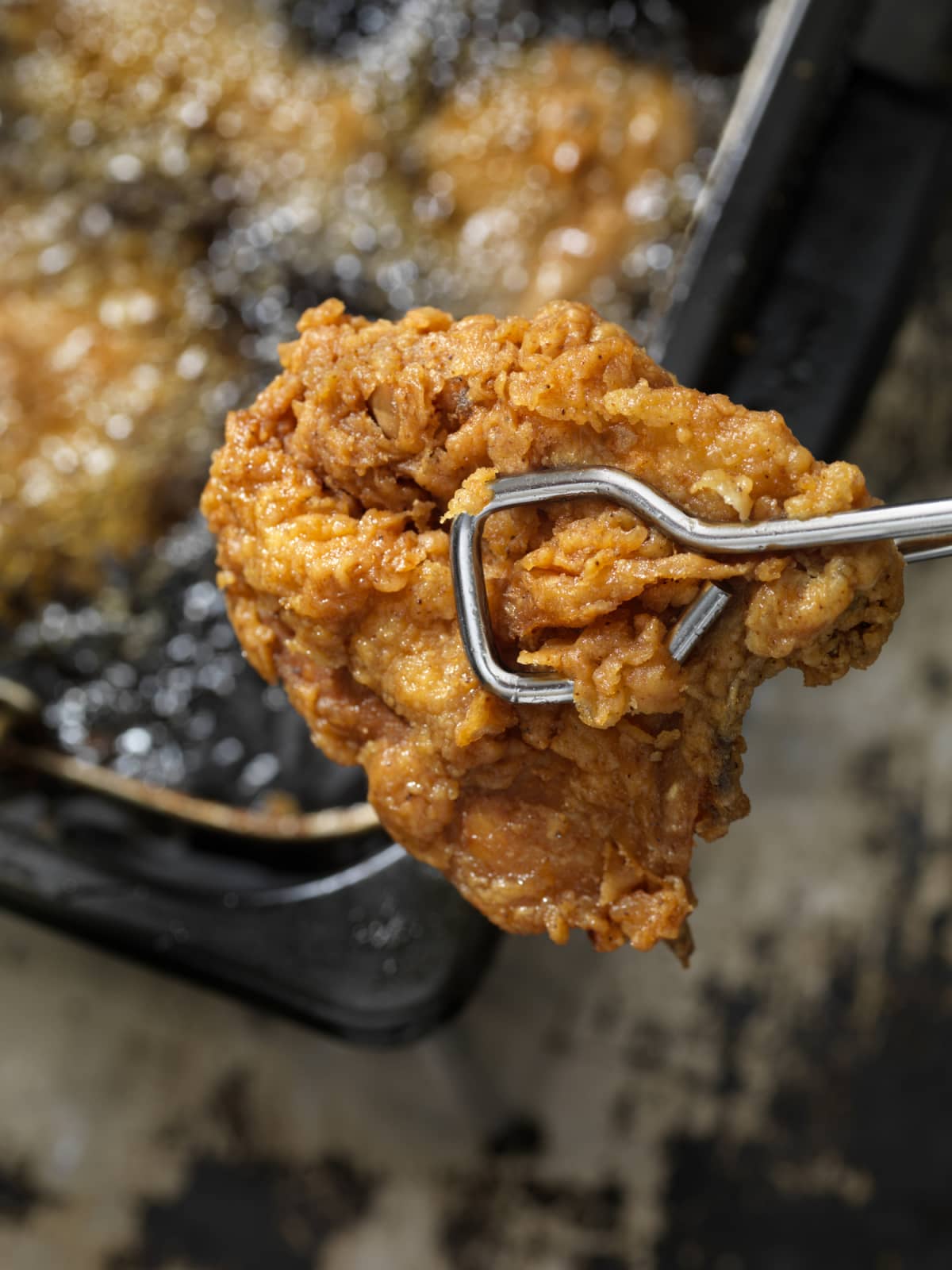 Piece of fried chicken held by tongs