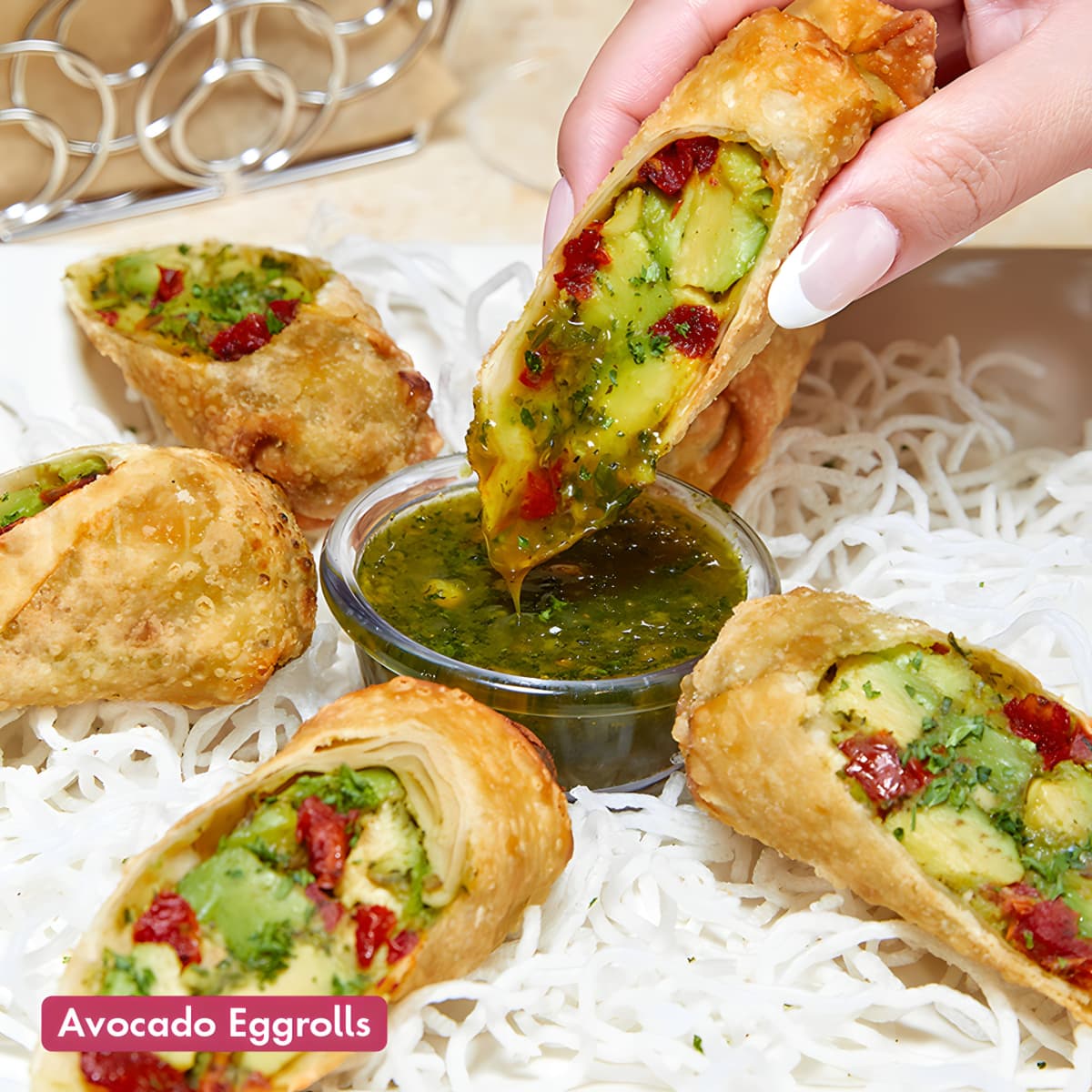 A hand dipping Cheesecake Factory's eggrolls into a green sauce