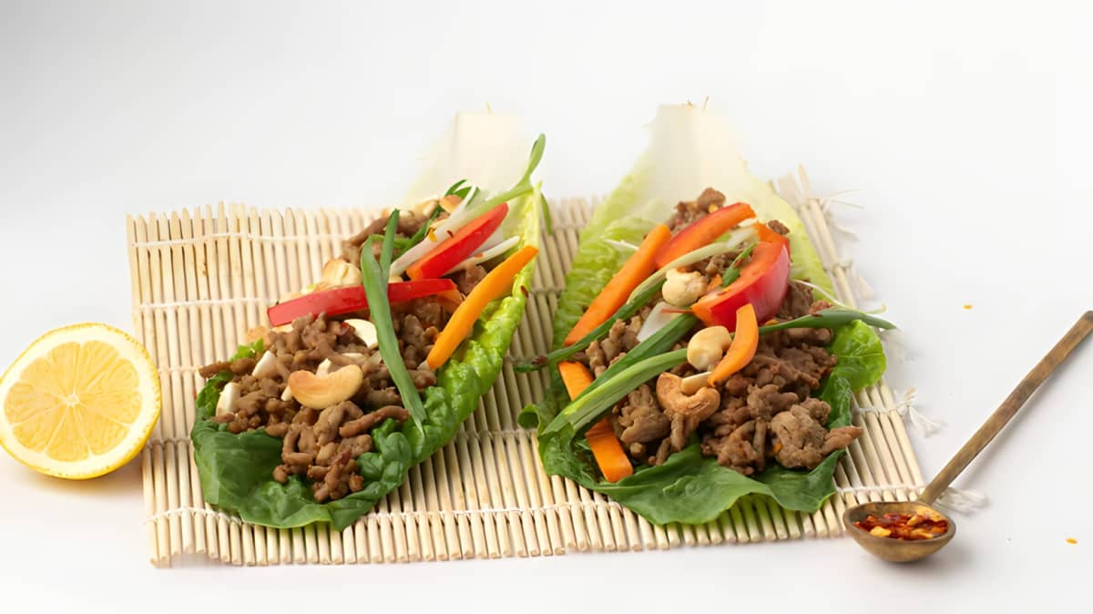 A lettuce wrap with meat, nuts, and peppers