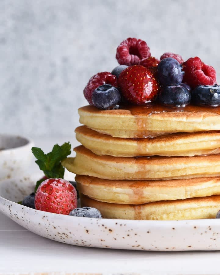 Stack of fluffy pancakes topped with berries and syrup
