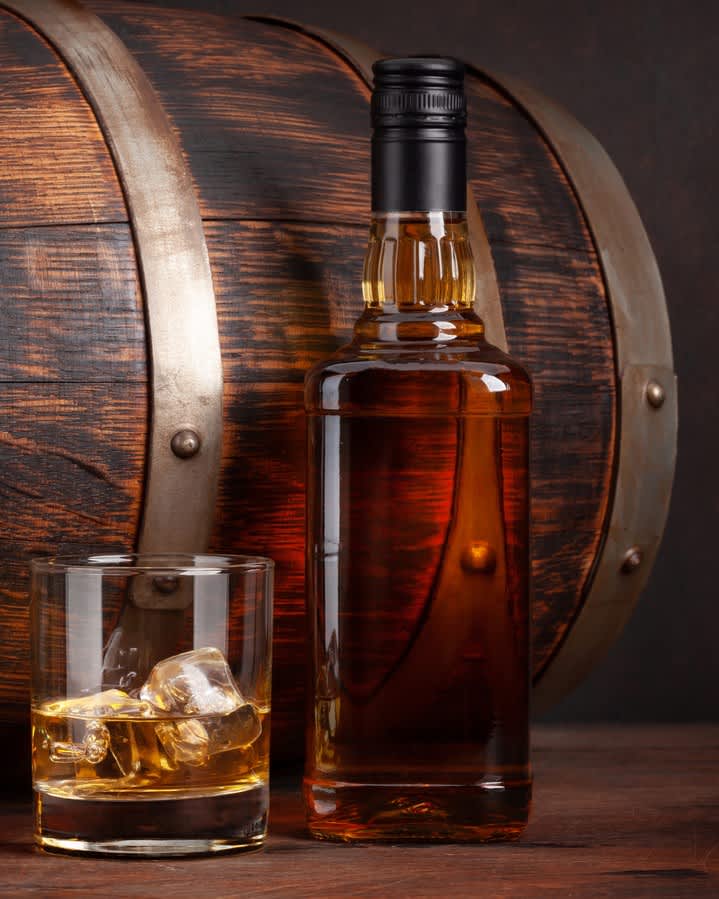 Bottle and glass of whiskey next to barrel