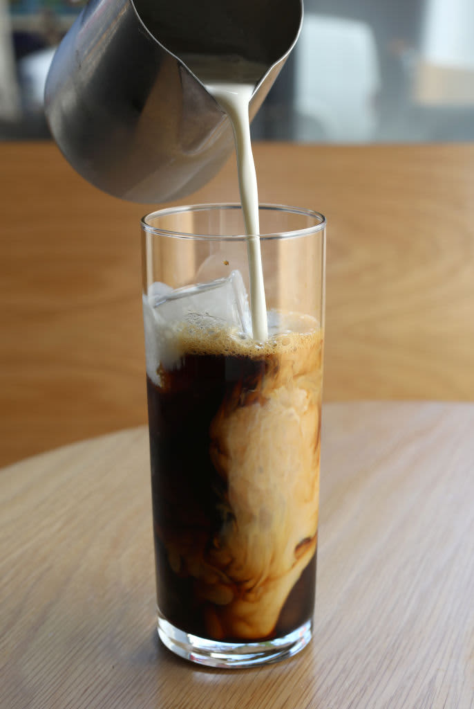 Creamer being poured into a tall glass of iced coffee