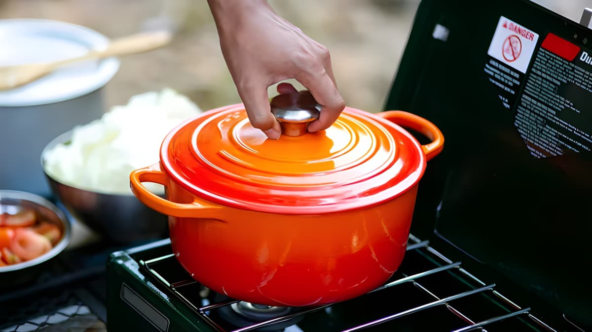 A person holding the lid of an orange Dutch oven.