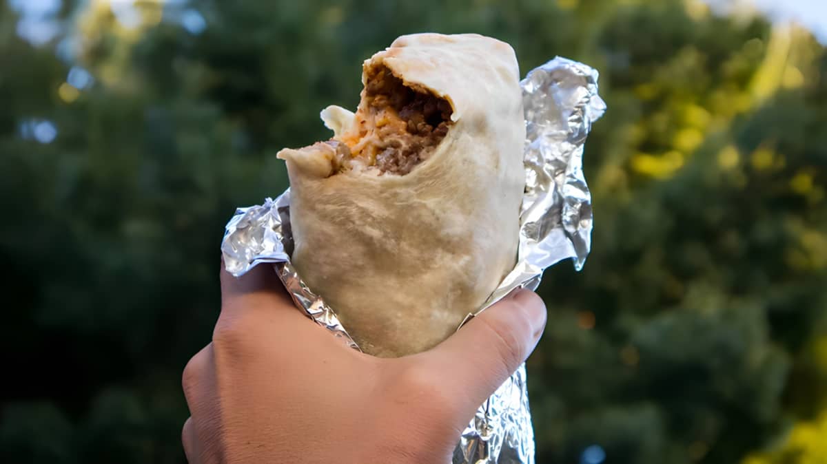 Hand holding burrito wrapped in foil