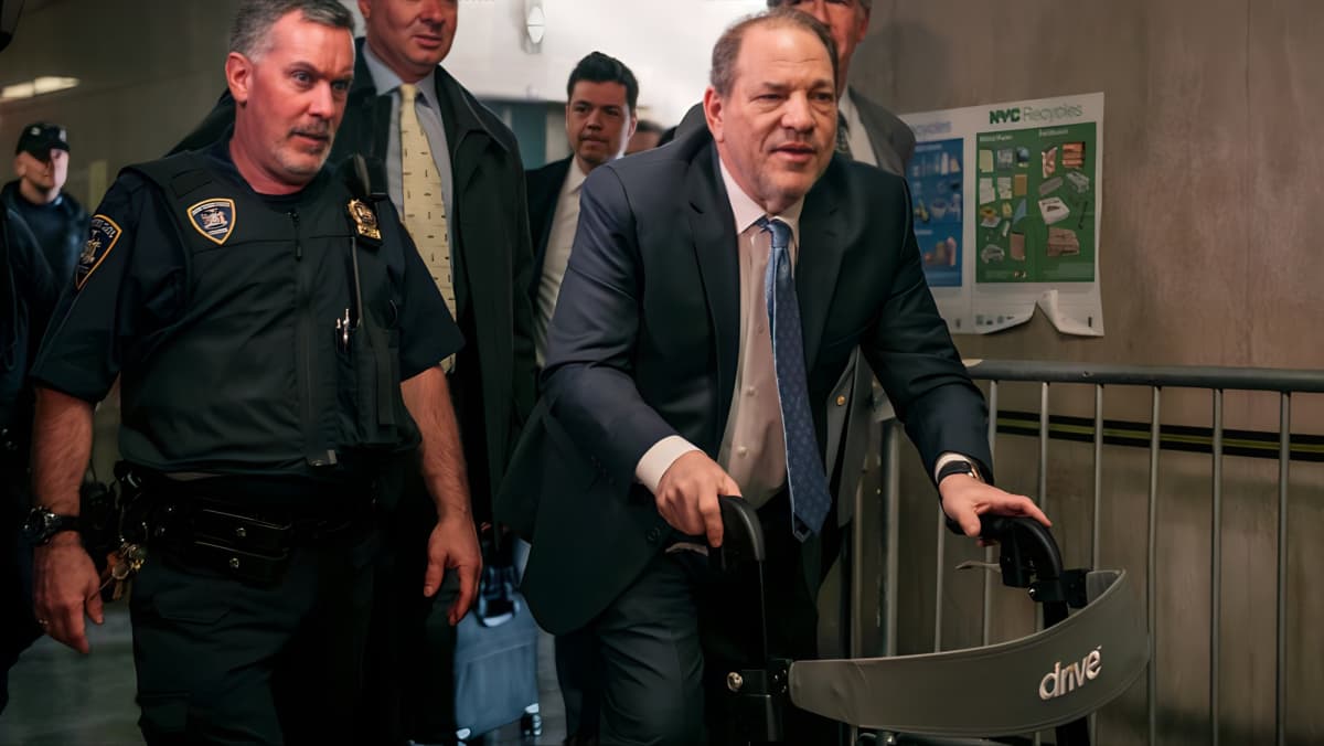 Harvey Weinstein walking beside a cop using a walker
