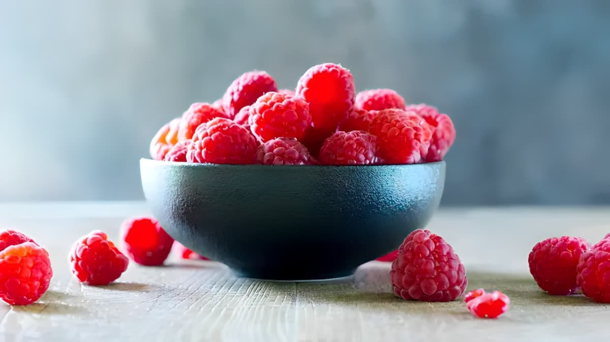 Raspberries in a bowl and on a table.