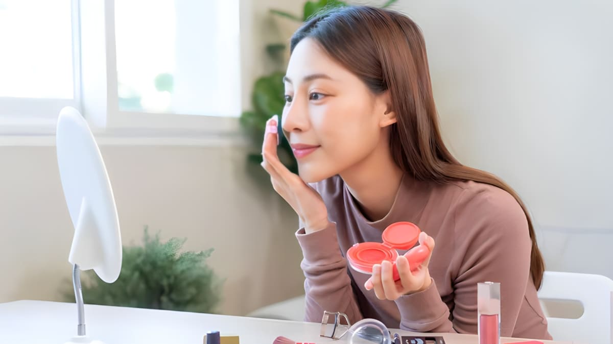 A woman applying red blush to her cheeks