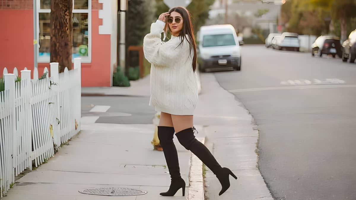 A woman walking and wearing a white oversized sweater and sunglasses