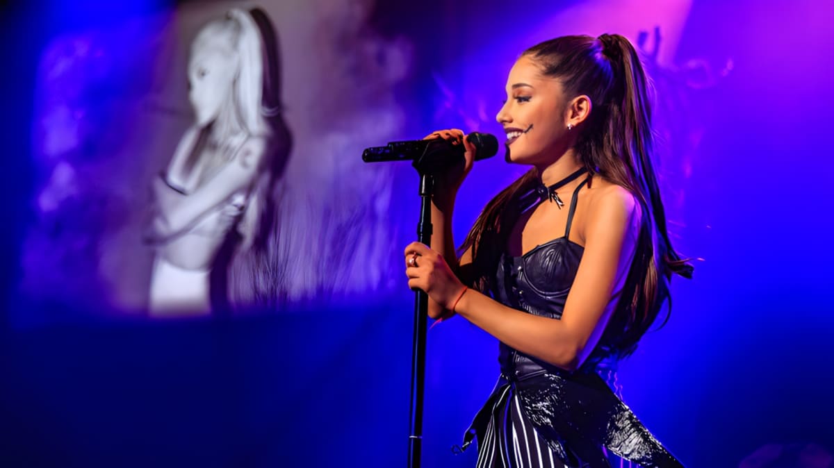 Ariana Grande with her iconic ponytail speaking into a mic