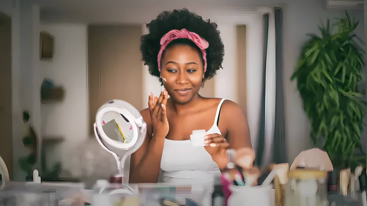 Woman applying cream to her face in front of a mirror.