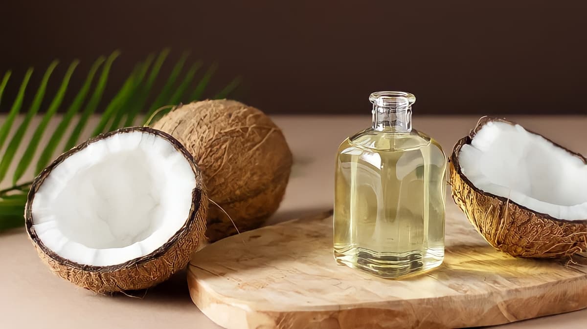 A bottle of oil next to half a coconut.